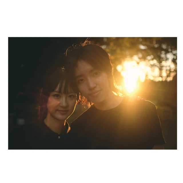 Portrait of a smiling young couple in an outdoor setting during golden hour, backlit by the sun, creating a warm, romantic atmosphere.