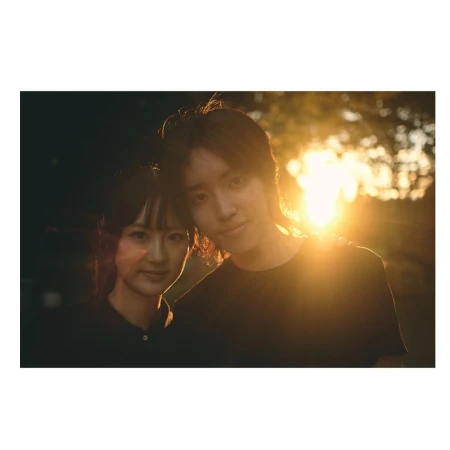 Portrait of a smiling young couple in an outdoor setting during golden hour, backlit by the sun, creating a warm, romantic atmosphere.
