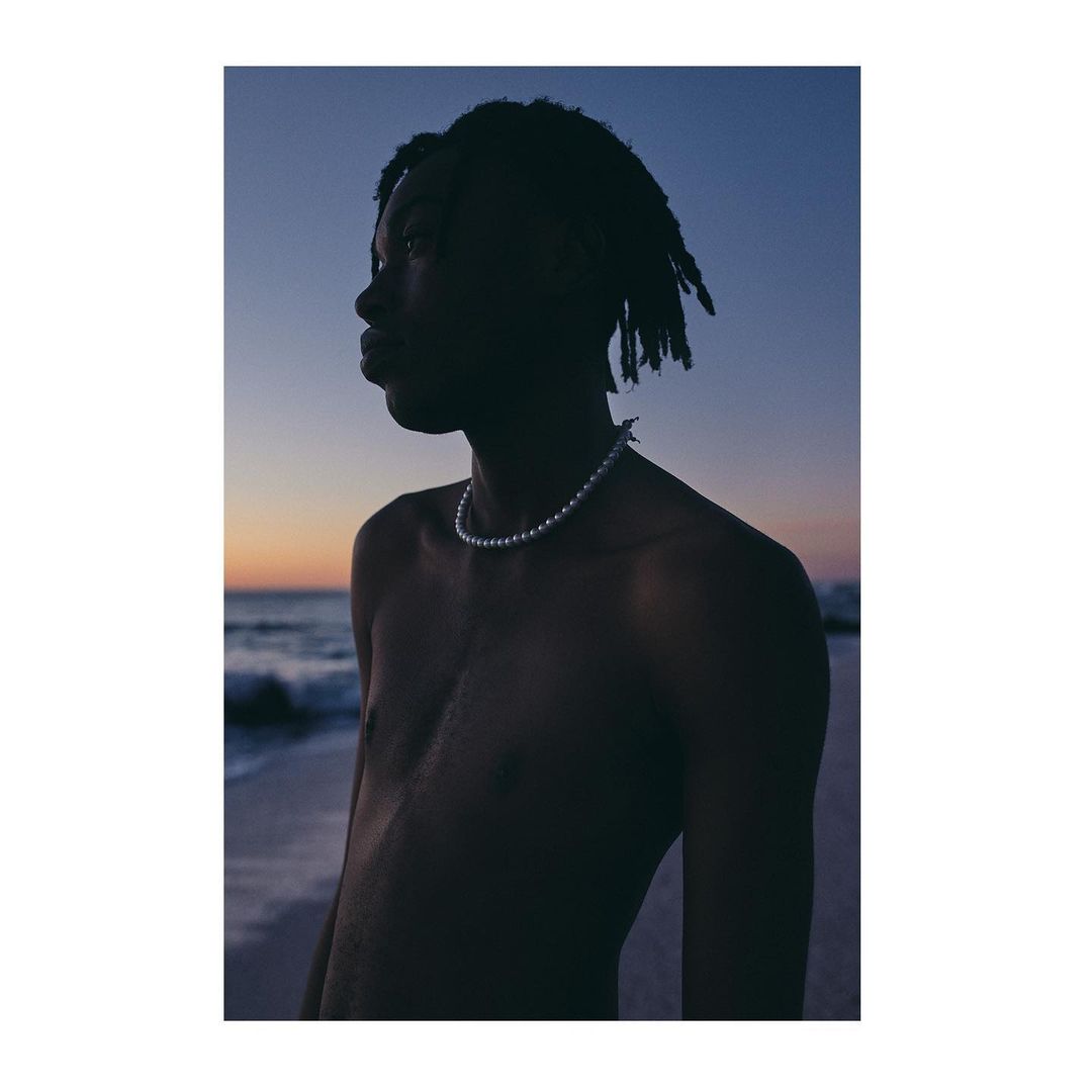 Portrait of a black man wearing a pearl necklace against a sunset beach and ocean background.