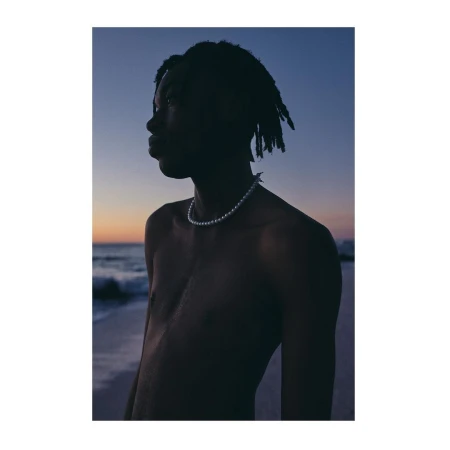 Portrait of a black man wearing a pearl necklace against a sunset beach and ocean background.