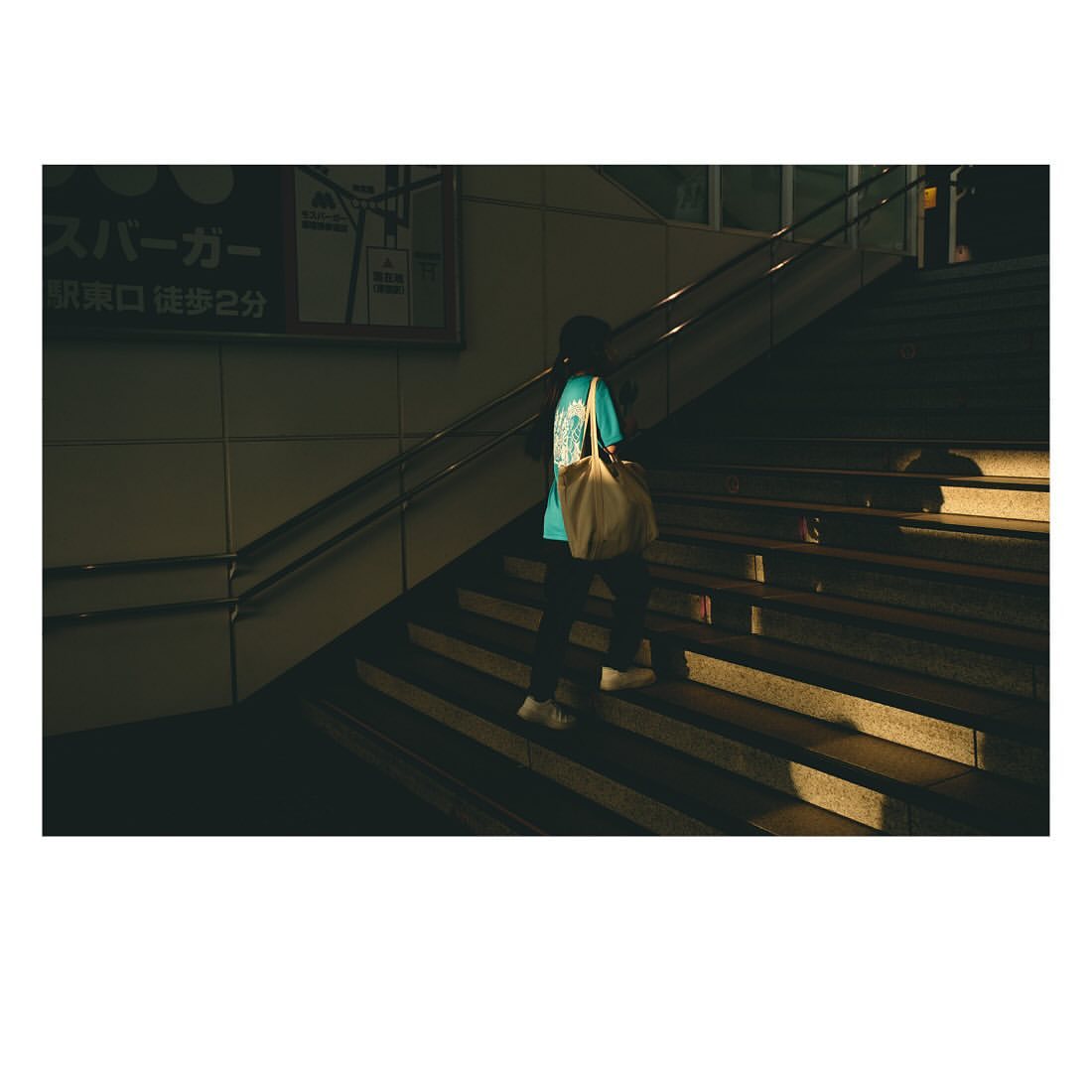 Person ascends outdoor stairs at night carrying a tote bag. The scene is illuminated by street lighting, casting shadows on the steps.