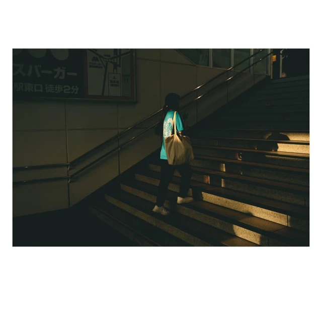 Person ascends outdoor stairs at night carrying a tote bag. The scene is illuminated by street lighting, casting shadows on the steps.