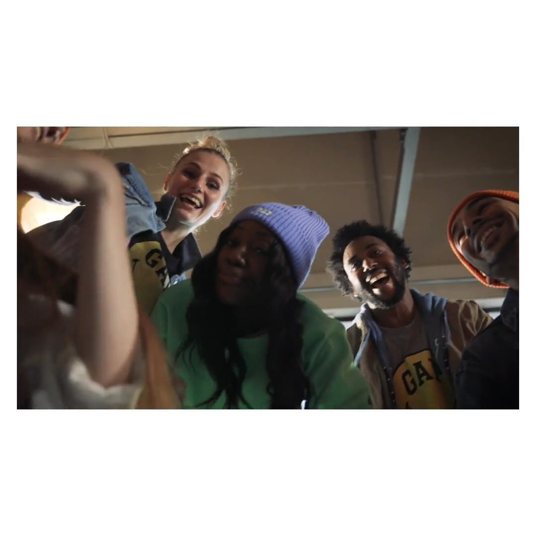 Diverse group of smiling people looking down at the camera, wearing casual clothing, including hats and a Gap-branded shirt, indoors.