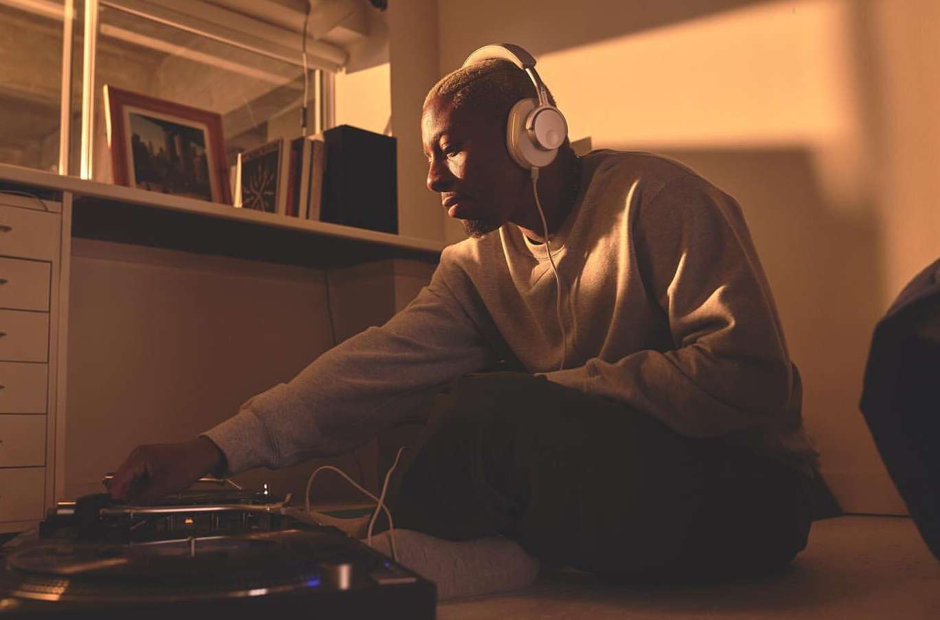 Person with headphones using turntable in warm-lit room. DJ mixing music indoors with record player and sound equipment.