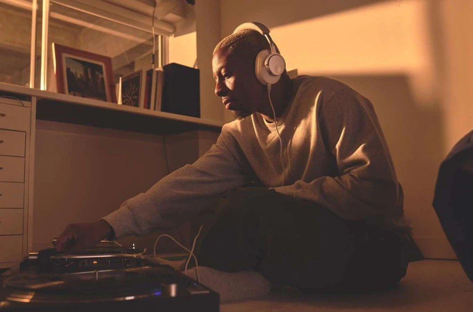 Person with headphones using turntable in warm-lit room. DJ mixing music indoors with record player and sound equipment.