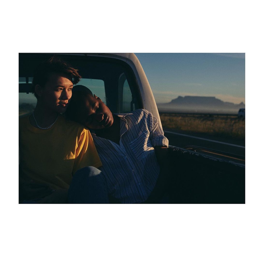 Two people in the bed of a pickup truck, with a mountain range in the background, creating a serene and intimate travel portrait.