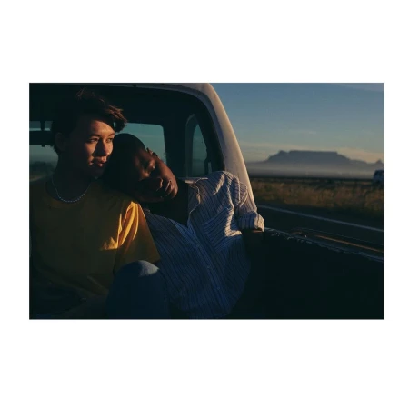 Two people in the bed of a pickup truck, with a mountain range in the background, creating a serene and intimate travel portrait.