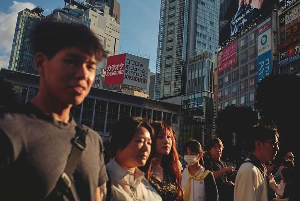 Street scene in Tokyo, Japan featuring a group of pedestrians, including adult men and women, walking in front of modern buildings.