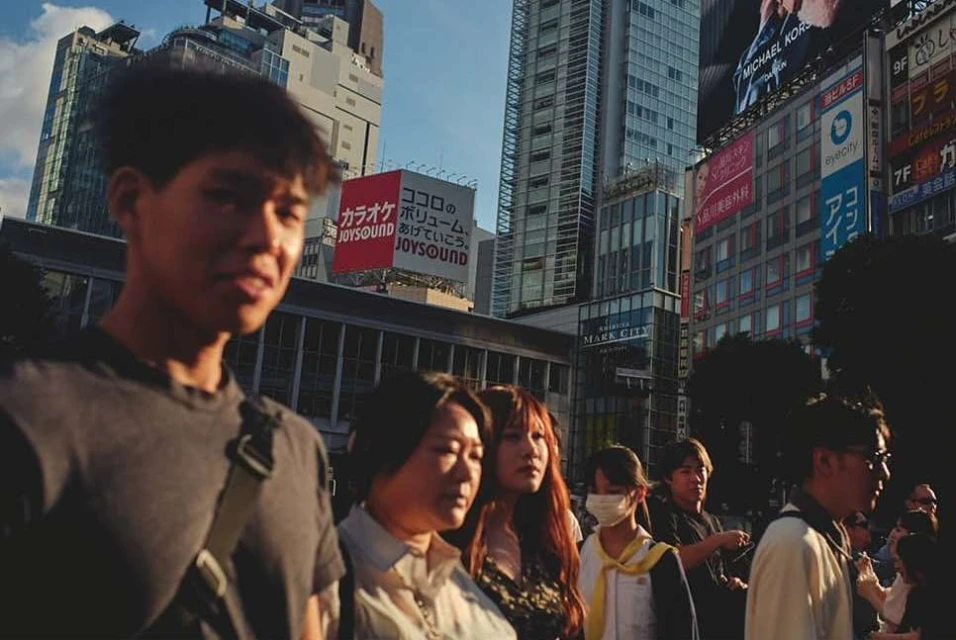Street scene in Tokyo, Japan featuring a group of pedestrians, including adult men and women, walking in front of modern buildings.
