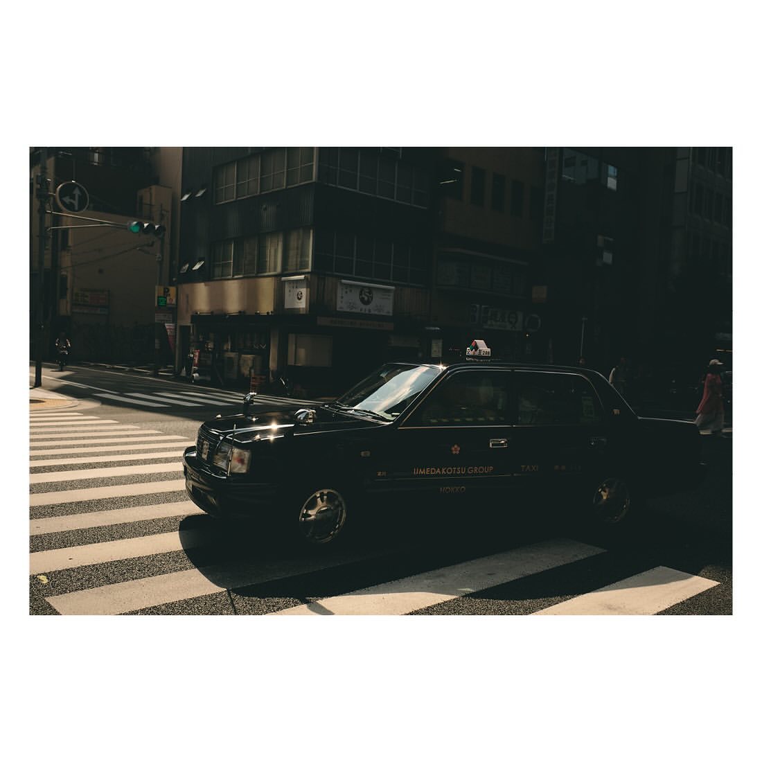 Black taxi cab driving on a city street crosswalk in urban Tokyo, Japan with buildings, city lights, and shadows.