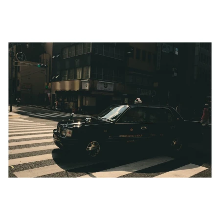 Black taxi cab driving on a city street crosswalk in urban Tokyo, Japan with buildings, city lights, and shadows.