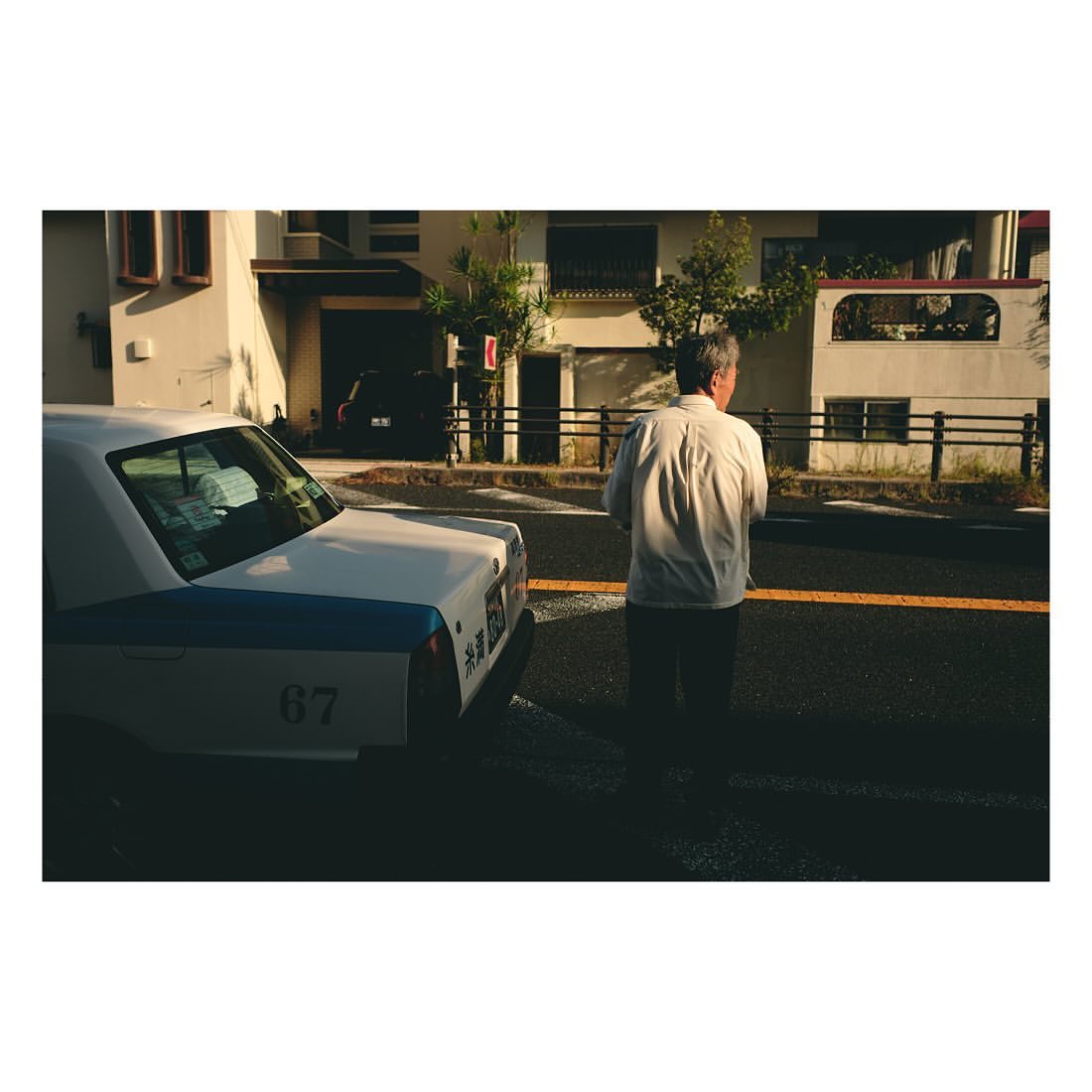 Mature man in a button-down shirt standing on a street with a white taxi and buildings in the background during daylight hours.
