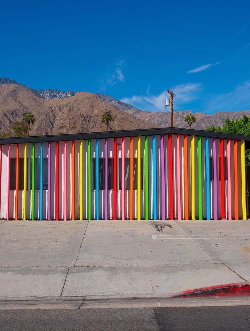 Facade of building with colorful vertical bars, mountains in background under blue sky in Palm Springs, California.