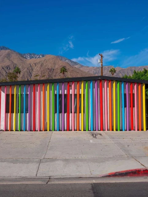 Facade of building with colorful vertical bars, mountains in background under blue sky in Palm Springs, California.