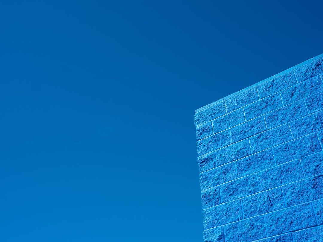 Blue brick wall under a clear sky, showcasing architectural detail and color contrast in an outdoor setting, bathed in daylight.