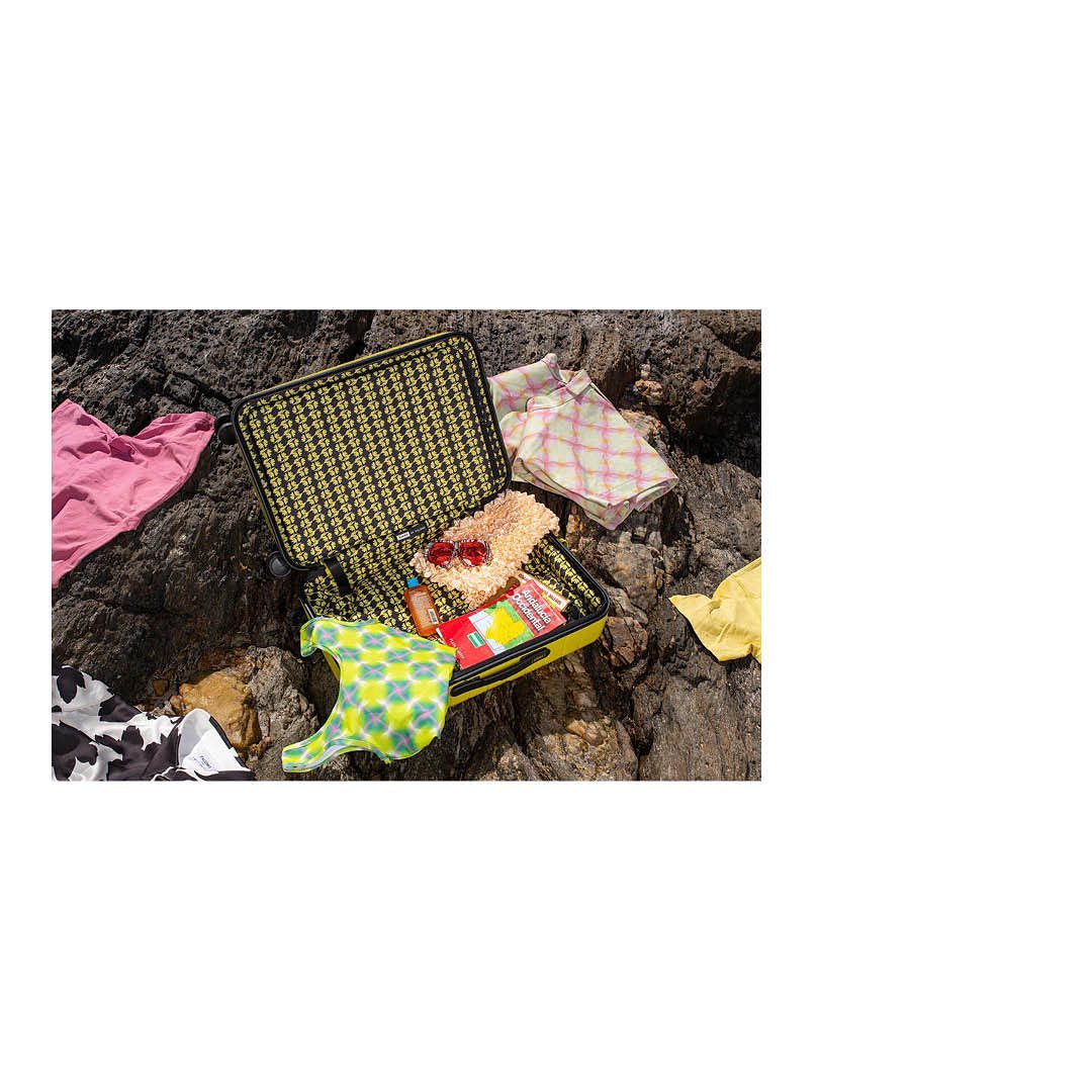 Open yellow suitcase with patterned interior, packed with clothes on rocky ground. Fashionable travel essentials and vacation concept.