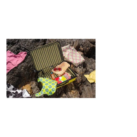 Open yellow suitcase with patterned interior, packed with clothes on rocky ground. Fashionable travel essentials and vacation concept.