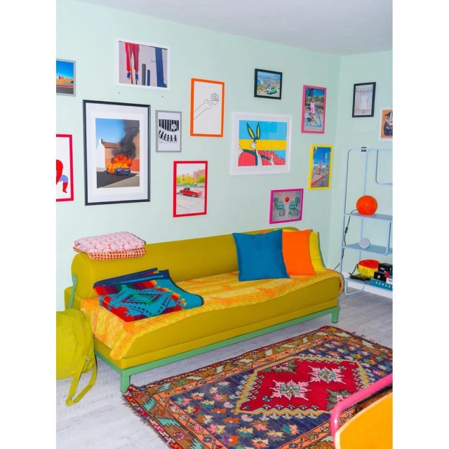 Living room scene with a yellow couch, colorful pillows, and graphic art on the wall, complemented by a patterned rug on the floor.
