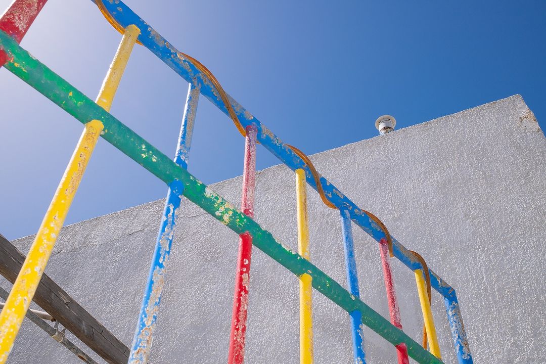 Colorful playground climbing frame against a clear blue sky and the side of a white building, shot from a low angle.