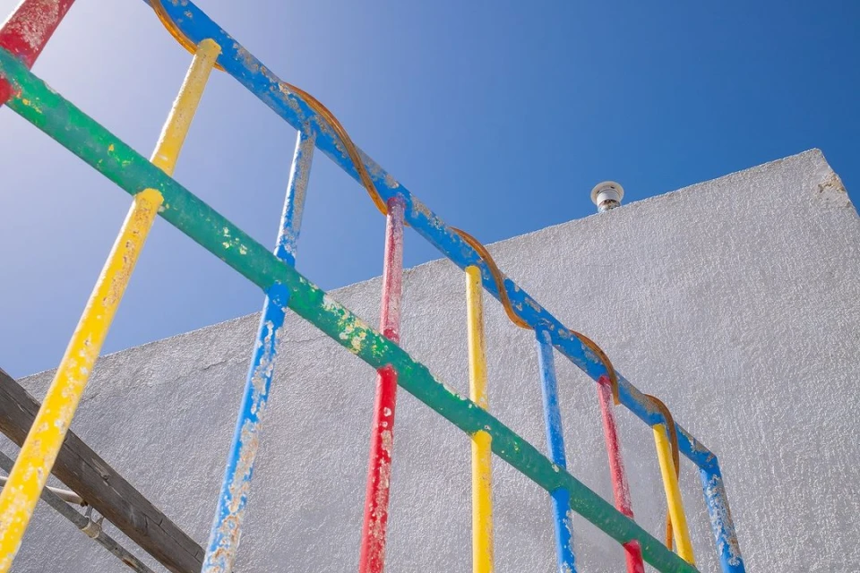 Colorful playground climbing frame against a clear blue sky and the side of a white building, shot from a low angle.