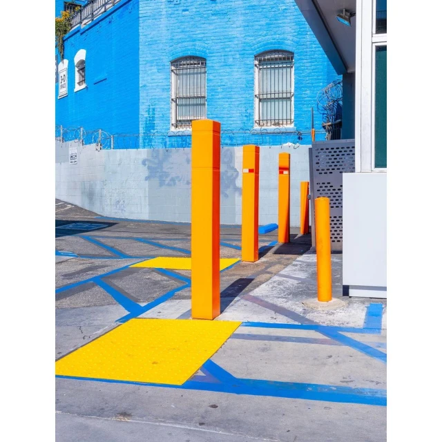 Exterior shot of orange bollards on a parking lot with a bright blue building and yellow and blue painted parking spaces, in daylight.