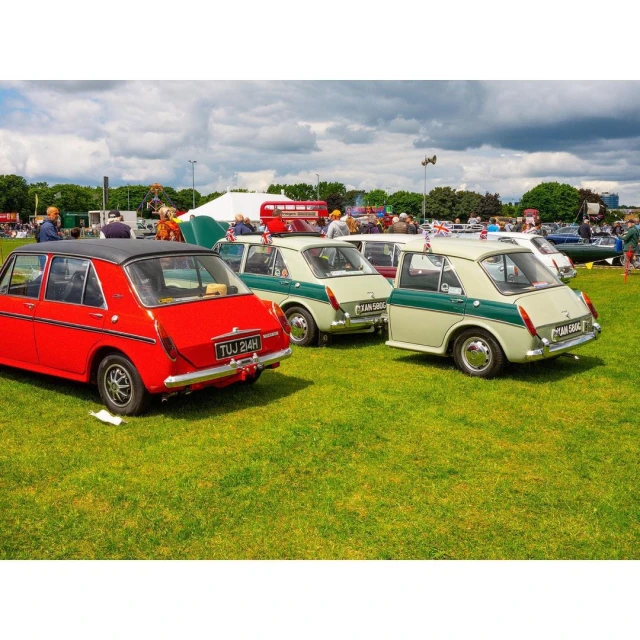 Several vintage cars parked on a grassy field under a cloudy sky, showcasing classic automotive designs in an outdoor setting.
