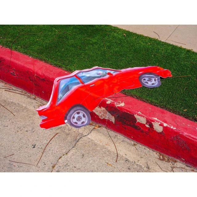 Red car artwork placed on concrete curb with grass background; vivid, playful automotive art.