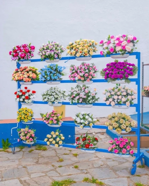 Floral display rack on a stone surface with several bouquets of flowers in vases. Variety of colors including pink, red, yellow, and white.