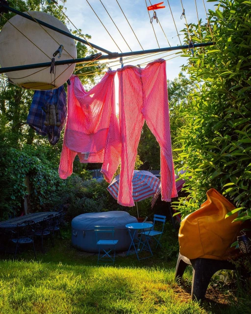 Outdoor clothesline with pink striped clothing, blue outdoor furniture, and green lawn in a backyard garden setting on a sunny day.