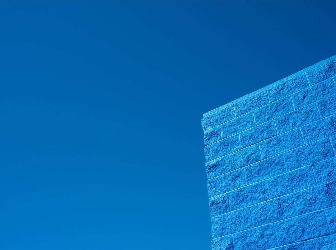 Low-angle shot of a blue brick wall against a clear blue sky, highlighting texture and color contrast.