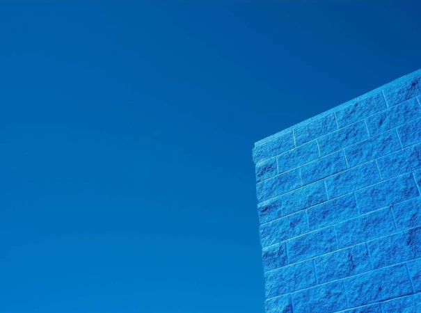Low-angle shot of a blue brick wall against a clear blue sky, highlighting texture and color contrast.