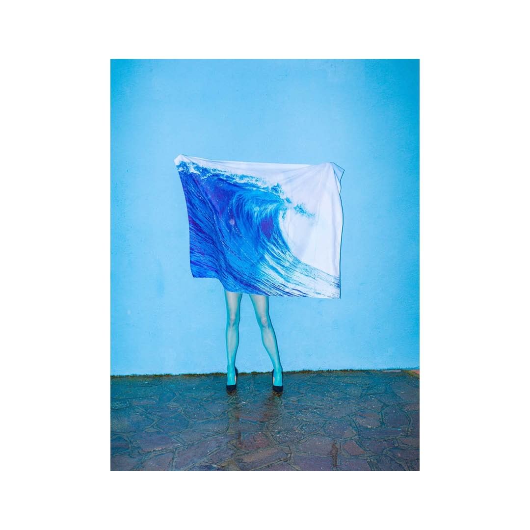 Fashion shot of an adult female posing with a blue and white wave-print textile in front of a blue wall, and wearing blue tights and black heels.