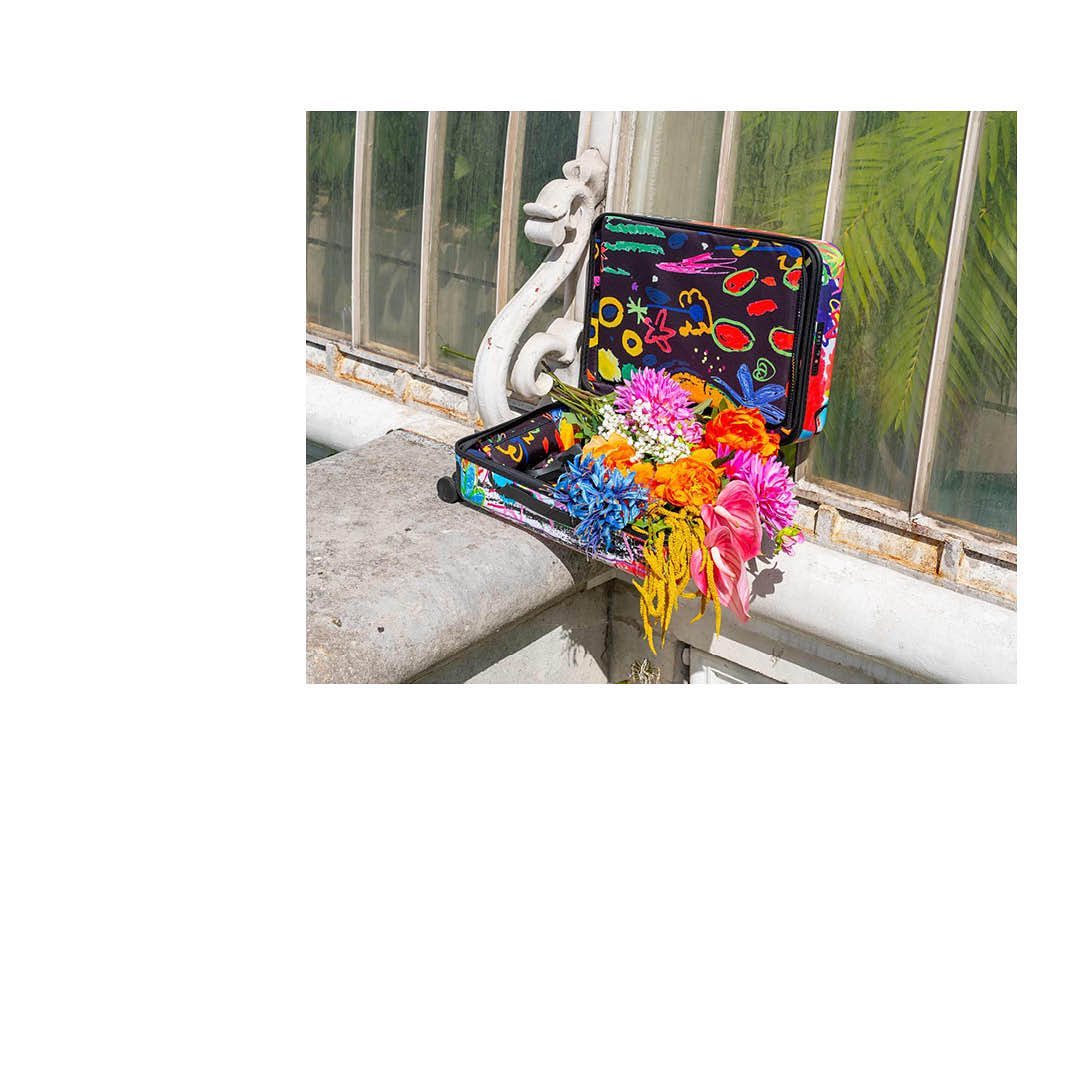 Open vintage suitcase filled with colorful flowers arranged on a stone ledge near a window, artistic composition.