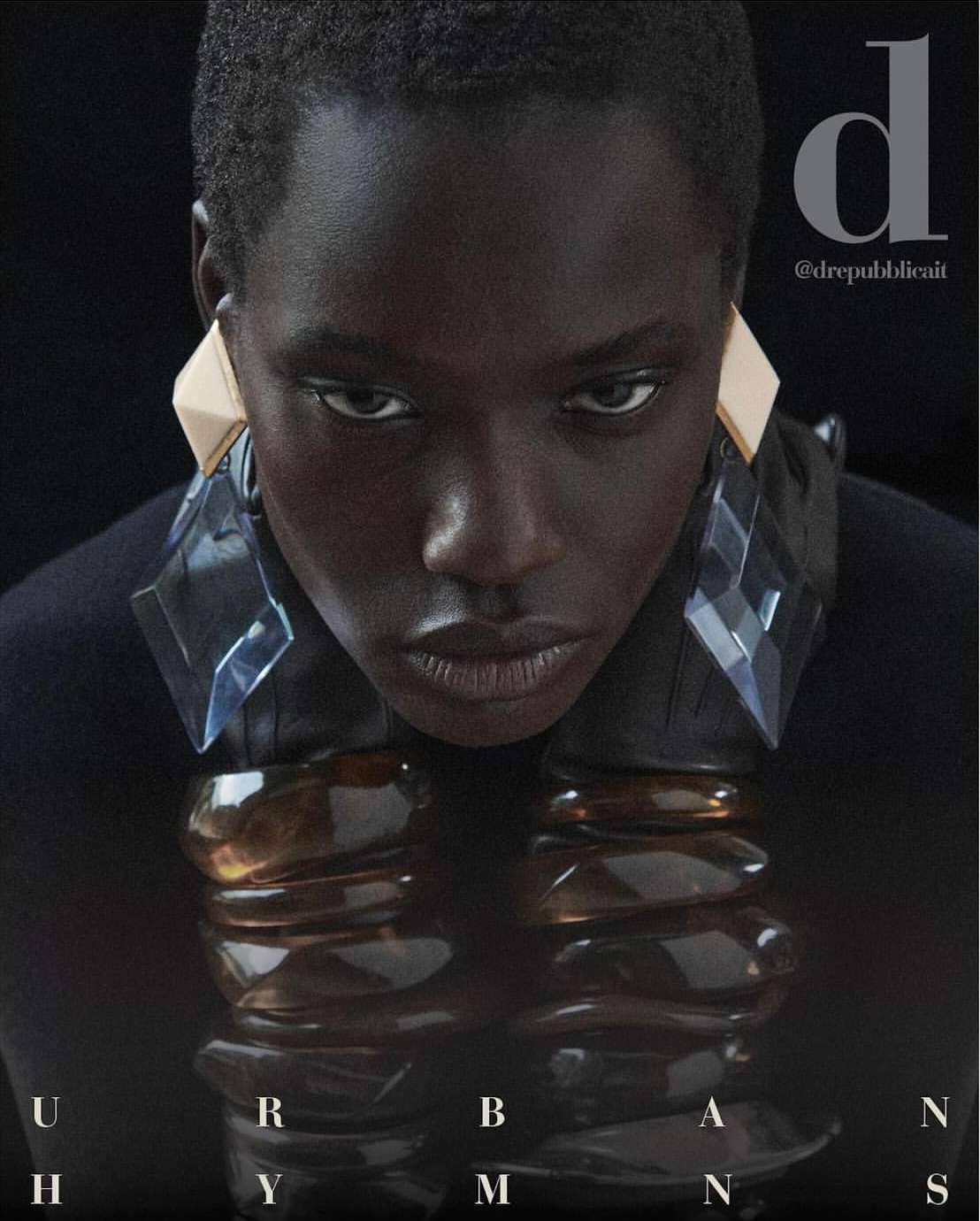 Close-up fashion shot of a dark-skinned model with geometric earrings and a collar necklace, set against a dark background. 