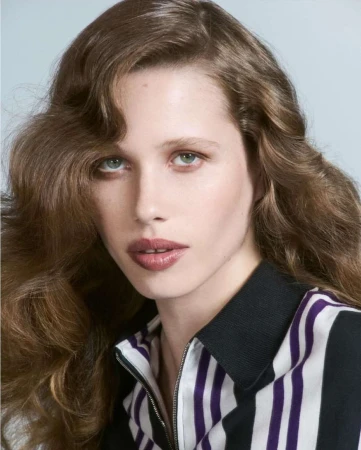 Close-up portrait of a woman with long wavy brown hair wearing a striped zip-up polo shirt in Paris.