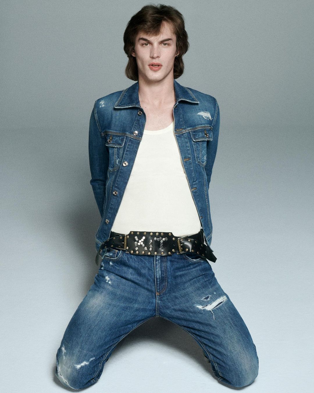 Male model in denim jacket and jeans kneeling against a grey backdrop photographed by Will Scarborough in Paris.