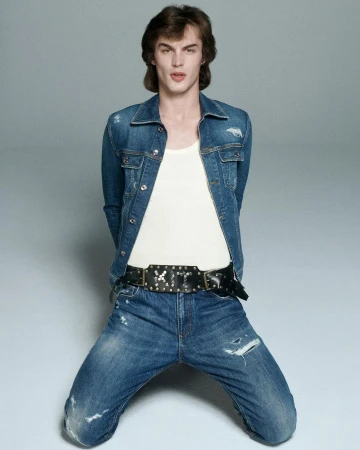 Male model in denim jacket and jeans kneeling against a grey backdrop photographed by Will Scarborough in Paris.