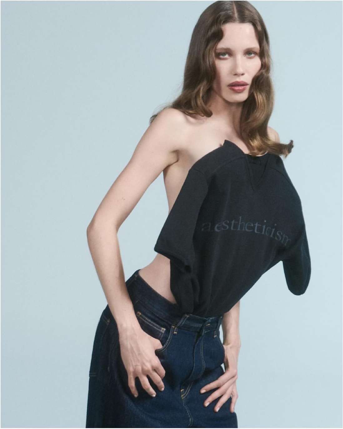 Model wearing dark denim jeans and a structured black top against a pale background photographed by Will Scarborough