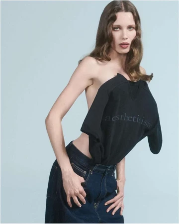Model wearing dark denim jeans and a structured black top against a pale background photographed by Will Scarborough