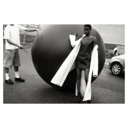 Black and white fashion editorial of a female model standing beside a large black inflatable sphere in an outdoor setting photographed by Will Scarborough in Paris.