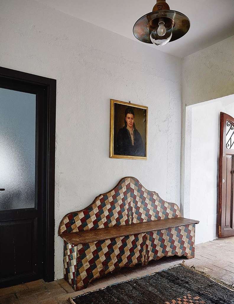 Hallway interior featuring a vintage wooden bench with a patterned design, a framed portrait on the wall, and a decorative overhead light.