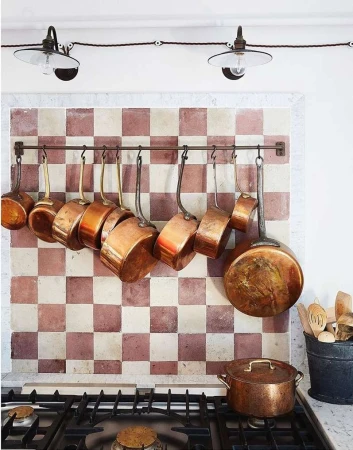 Kitchen interior with copper cookware hanging on a tile backsplash above a gas range, lit by overhead lamps, creating a warm, inviting space.