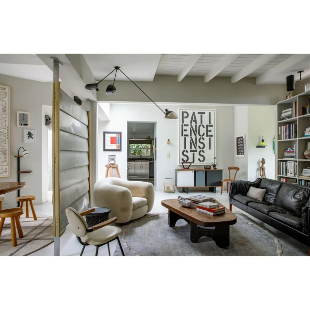 Living room interior featuring a black sofa, tan armchair, wood coffee table, and a 'Patience' typography poster, creating a stylish and modern space.