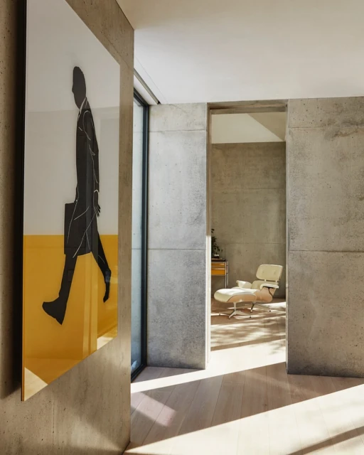 Modern interior with concrete walls, light wood floors, and artwork depicting a figure in a suit and tie, with light filtering in.