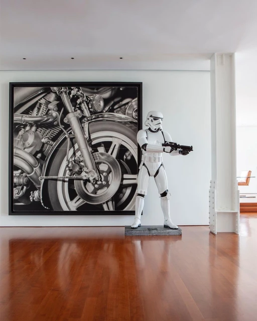 Indoor view of a Stormtrooper figurine standing near a framed black and white photograph of a motorcycle engine on a wood floor.