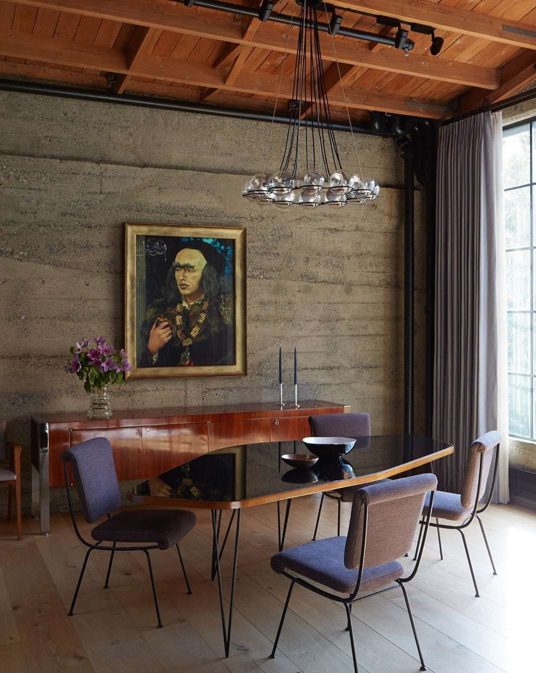 Dining room interior with modern furniture, artwork, and lighting fixture, featuring a table set for a meal with chairs, and wooden floors.