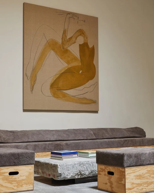 Minimalist interior featuring a yellow figure art piece, a grey sofa and ottomans, and a concrete coffee table with books.