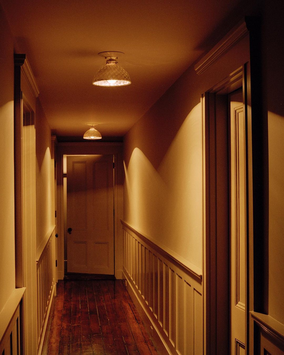 Interior shot of a hallway with wood floors, paneled walls, and overhead lighting creating warm, inviting illumination along the corridor.