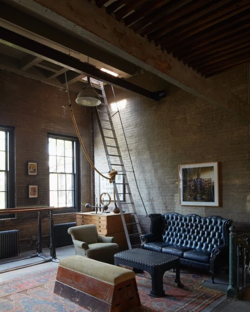 Interior of a vintage-style industrial space featuring a black leather sofa, armchair, exercise equipment, and exposed brick walls.