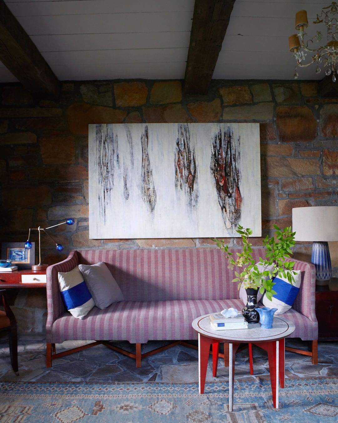 Interior view of a living room with a striped sofa, round accent table, and stone wall, illuminated by natural light.
